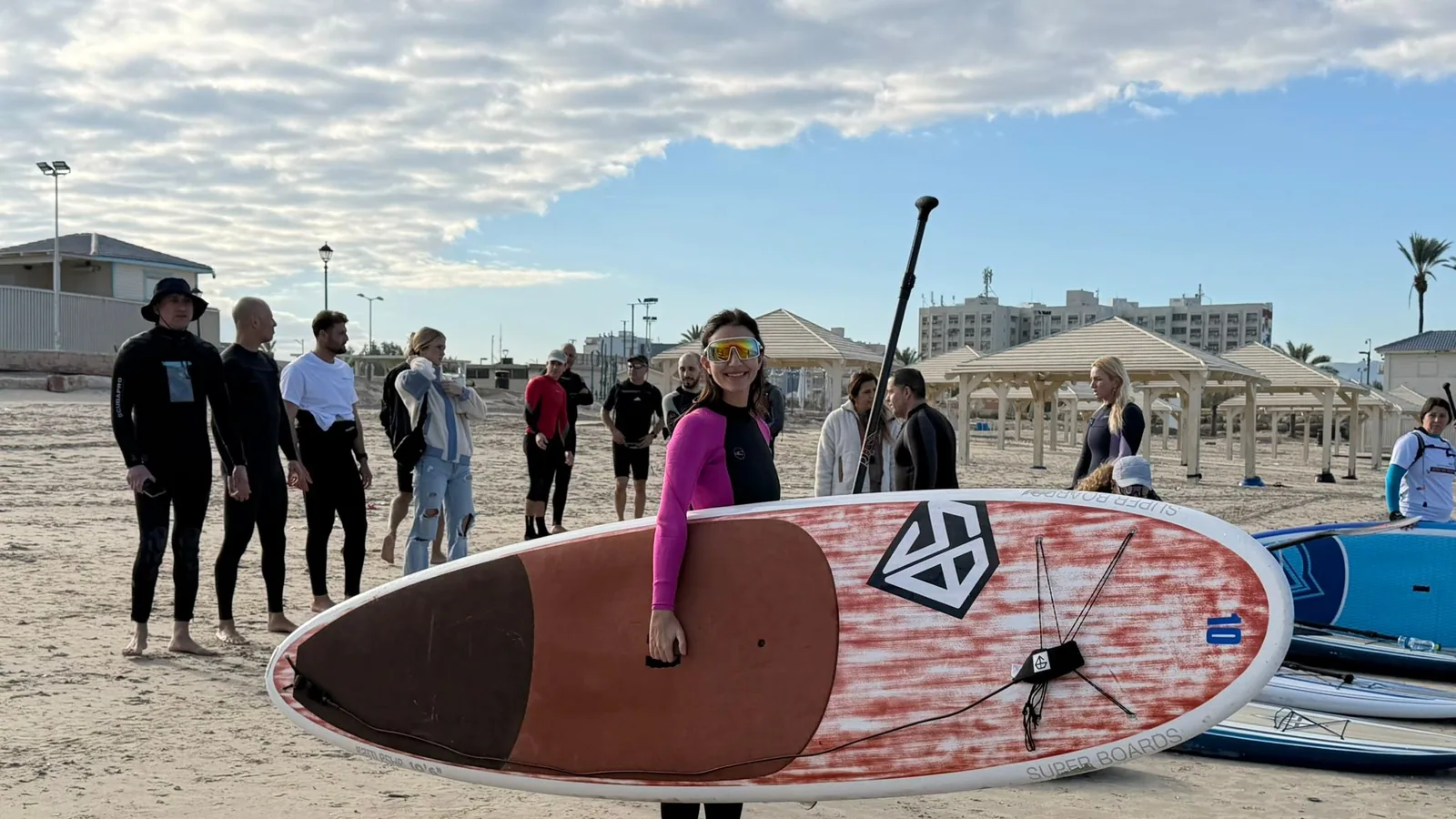 אישה מחזיקה גלשן סאפ של Super Boards בחוף הים במהלך פעילות קבוצתית