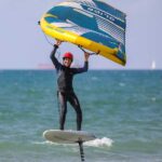 גולש מחייך מרחף על גלשן ווינג פויל בים עם כנף צהובה-כחולה של Ocean Rodeo