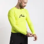 גולש לובש חולצת לייקרה צהובה לגלישה עם שרוול ארוך של המותג Rusty