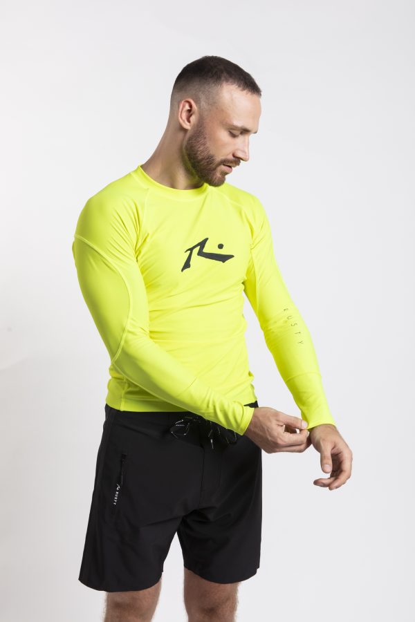 גולש לובש חולצת לייקרה צהובה לגלישה עם שרוול ארוך של המותג Rusty